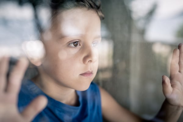 one-sad-little-boy-standing-near-the-window-at-PL25REZ